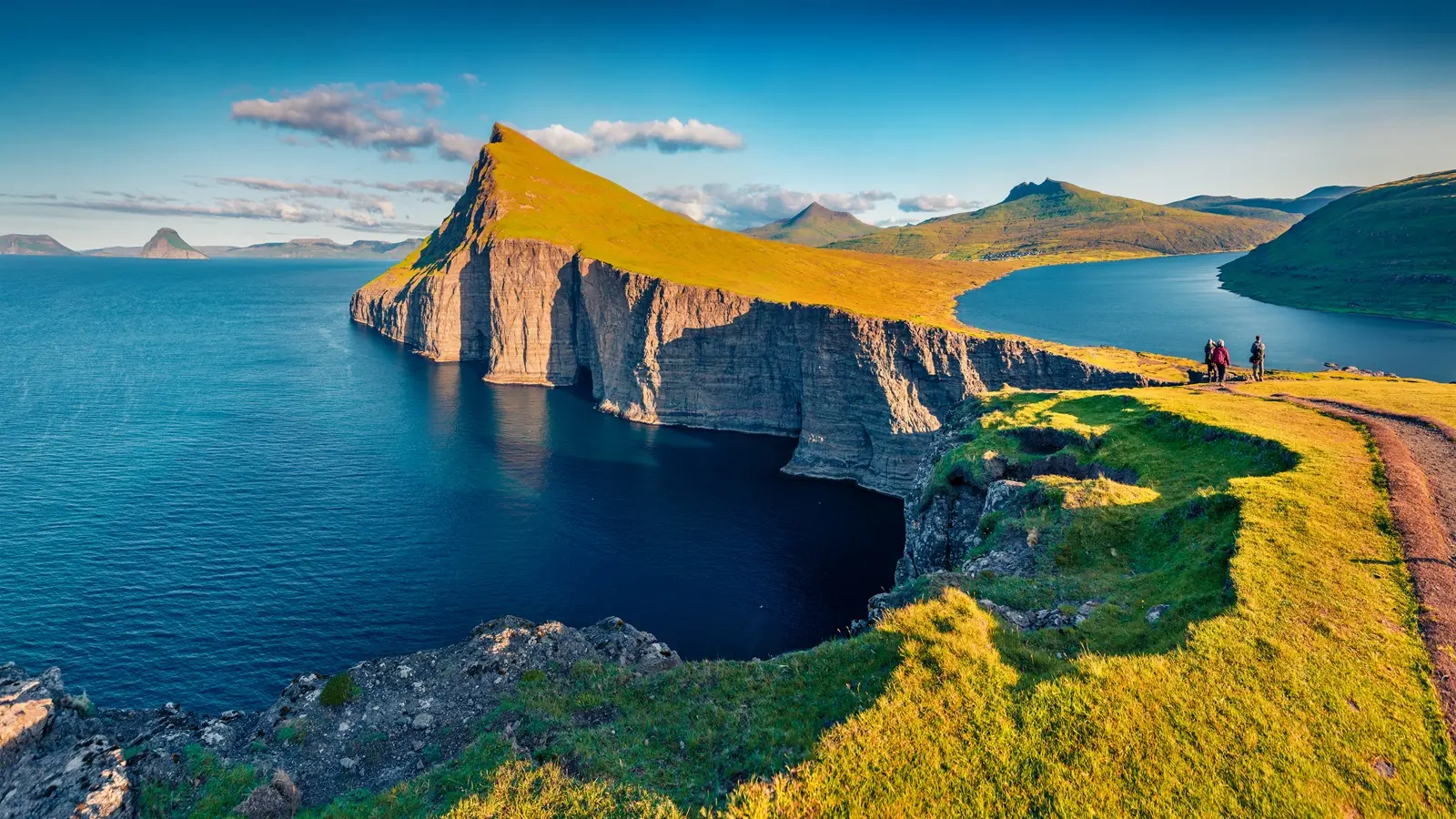 Hikers on the trail to Sørvágsvatn with the lake appearing above the Atlantic Ocean in the Faroe Islands
