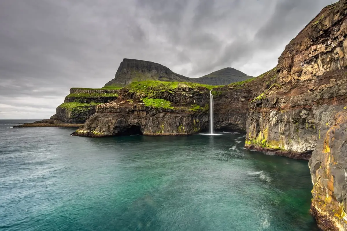 Múlafossur Waterfall in bright daylight with Gásadalur village and mountains in the Faroe Islands