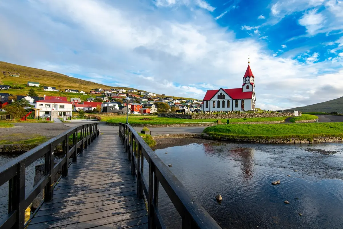 Person walking on bridge across the lake toward Sandavágur church.