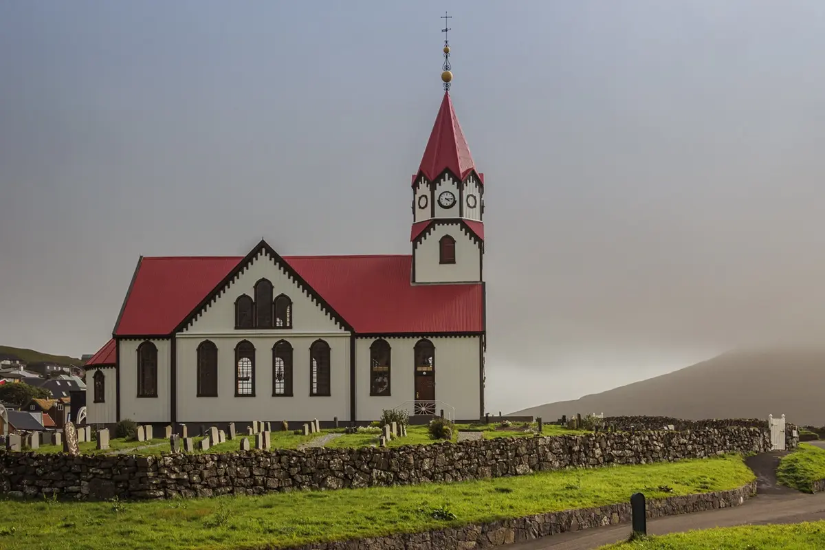 Sandavágur church and graveyard with stone walls under a cloudy sky.