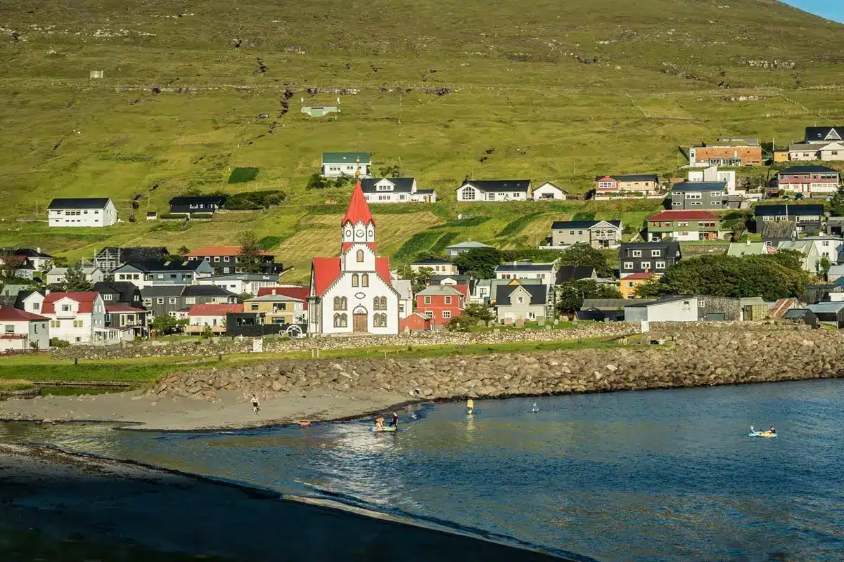 Children playing with inflatable boats in the sea near Sandavágur church.