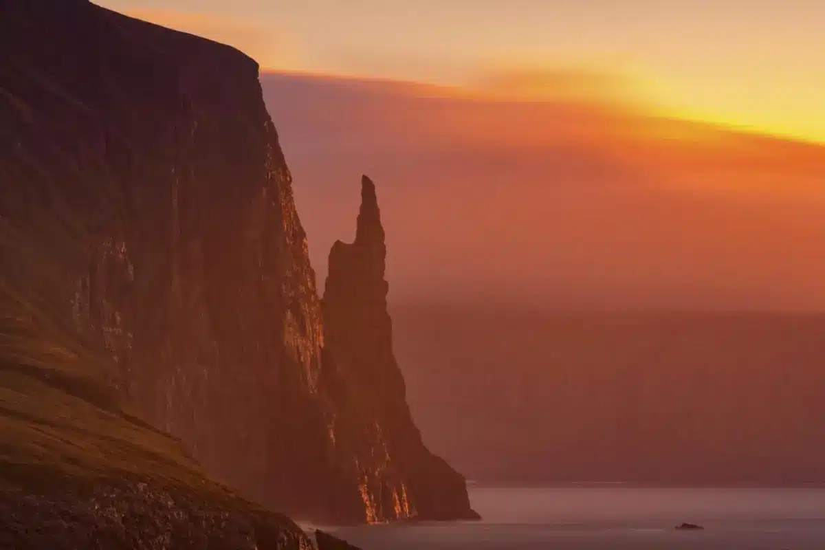 Trøllkonufingur sea stack rising from the ocean at sunset.